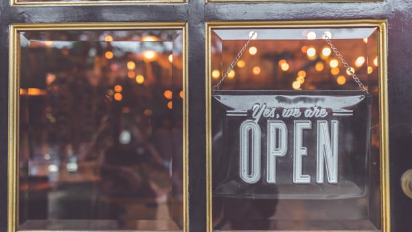 A sign on a glass door reads "Yes, we are open," with warm lights reflecting in the background, offering a comforting beacon even in these pandemic times.