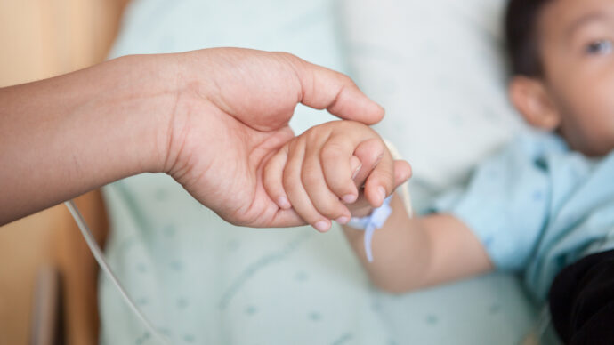 A physician gently holds a child's hand, connected to a medical tube, highlighting the long-term effects of compassionate care.