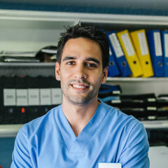 A person in blue scrubs stands in front of shelves with folders, smiling at the camera, embodying the positive results often seen in patient satisfaction surveys.