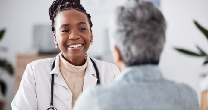 The future of the NHS gleams brightly as a doctor, clad in a white coat and stethoscope, smiles warmly while speaking with a patient in an office setting.