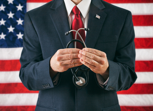 A person in a suit holds a stethoscope, symbolizing adherence to the Goldwater Rule, in front of an American flag.