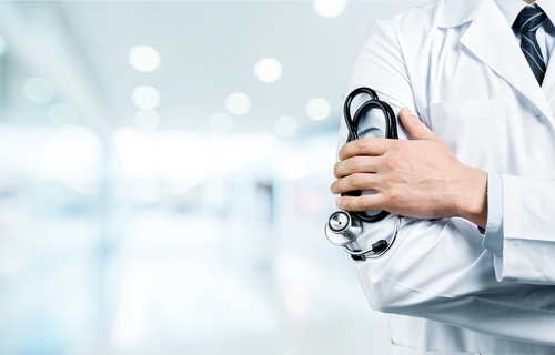 In a bright hospital hallway, a dedicated doctor in a white coat stands confidently with arms crossed, skillfully holding a stethoscope.