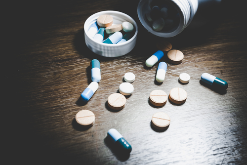 An open bottle with various pills, including capsules and tablets, is scattered on a wooden surface, highlighting the threat of counterfeit drugs lurking in plain sight.