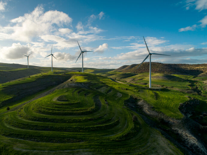 A landscape with four wind turbines on rolling green hills under a partly cloudy sky, symbolizing action today for a better tomorrow.