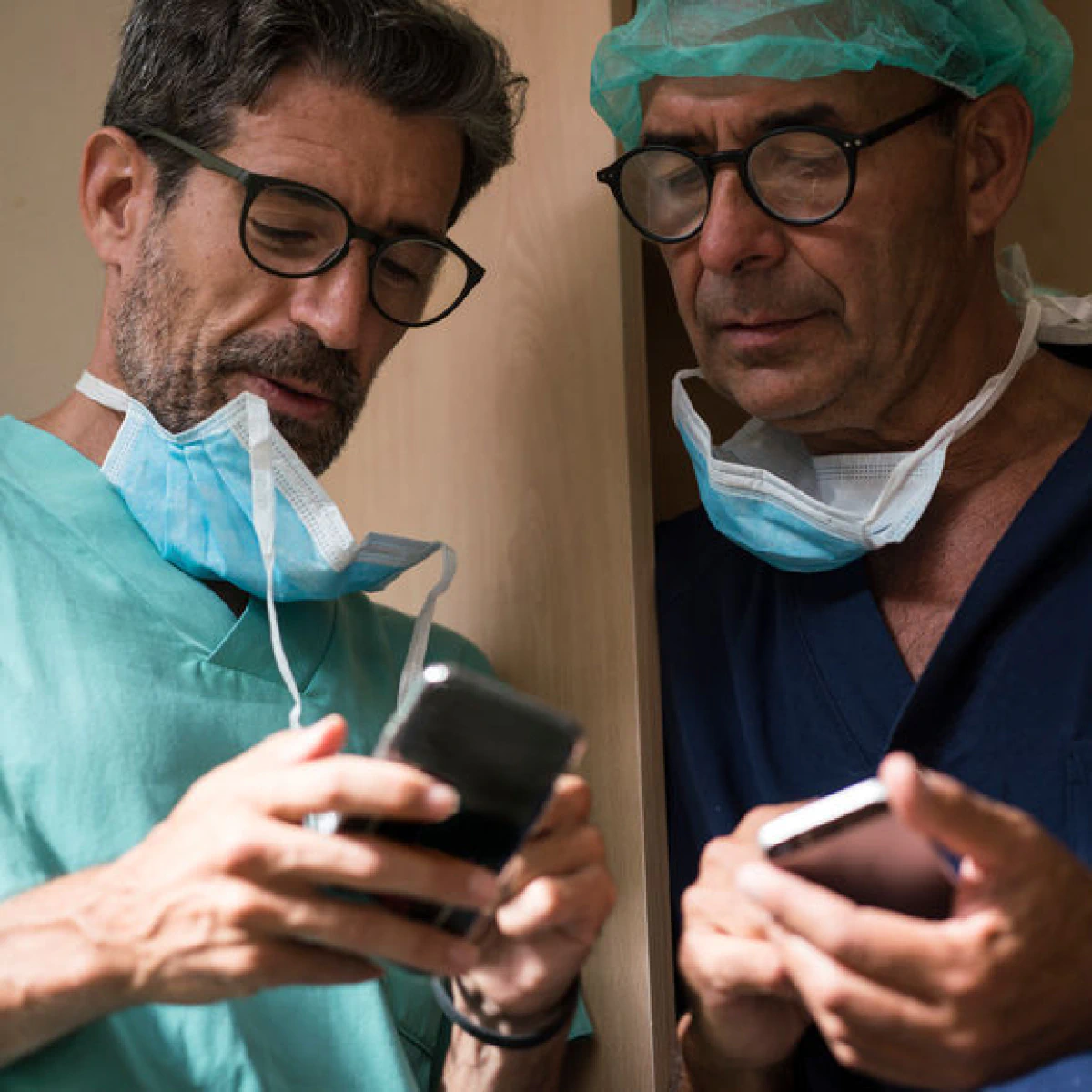 Dos profesionales sanitarios con uniformes y mascarillas miran sus teléfonos inteligentes.